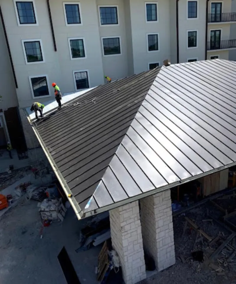 Crew installing standing seam metal roof panels on a commercial project in Pella